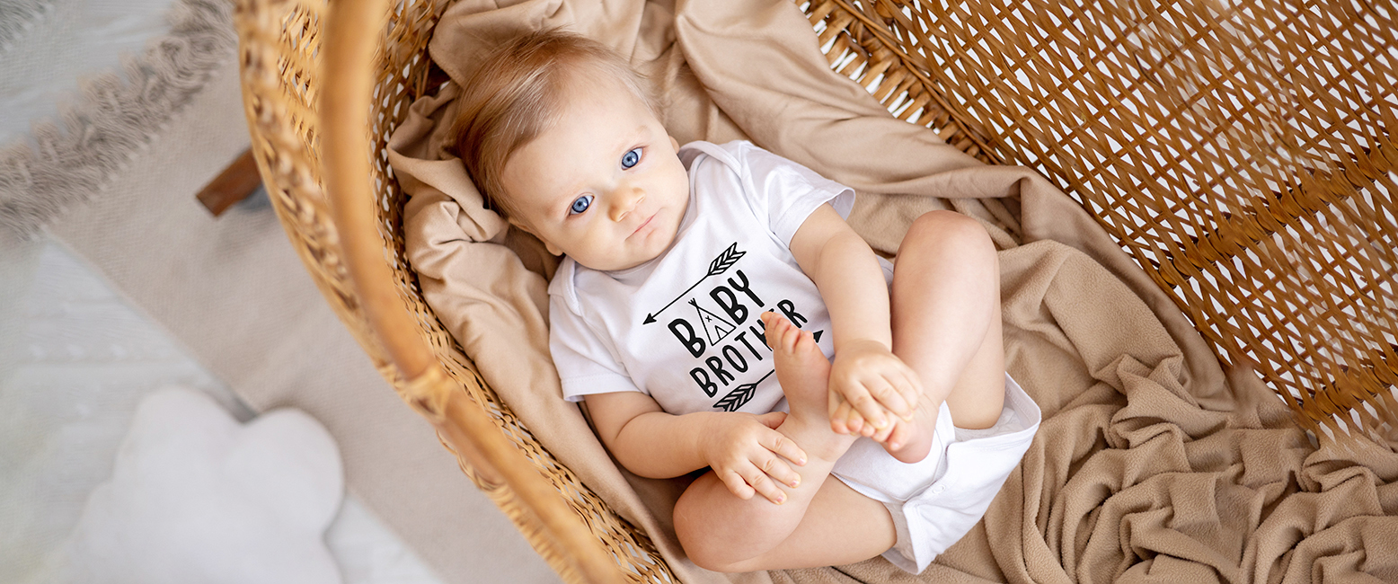 Baby brother in a personalised bodysuit lying in a crib